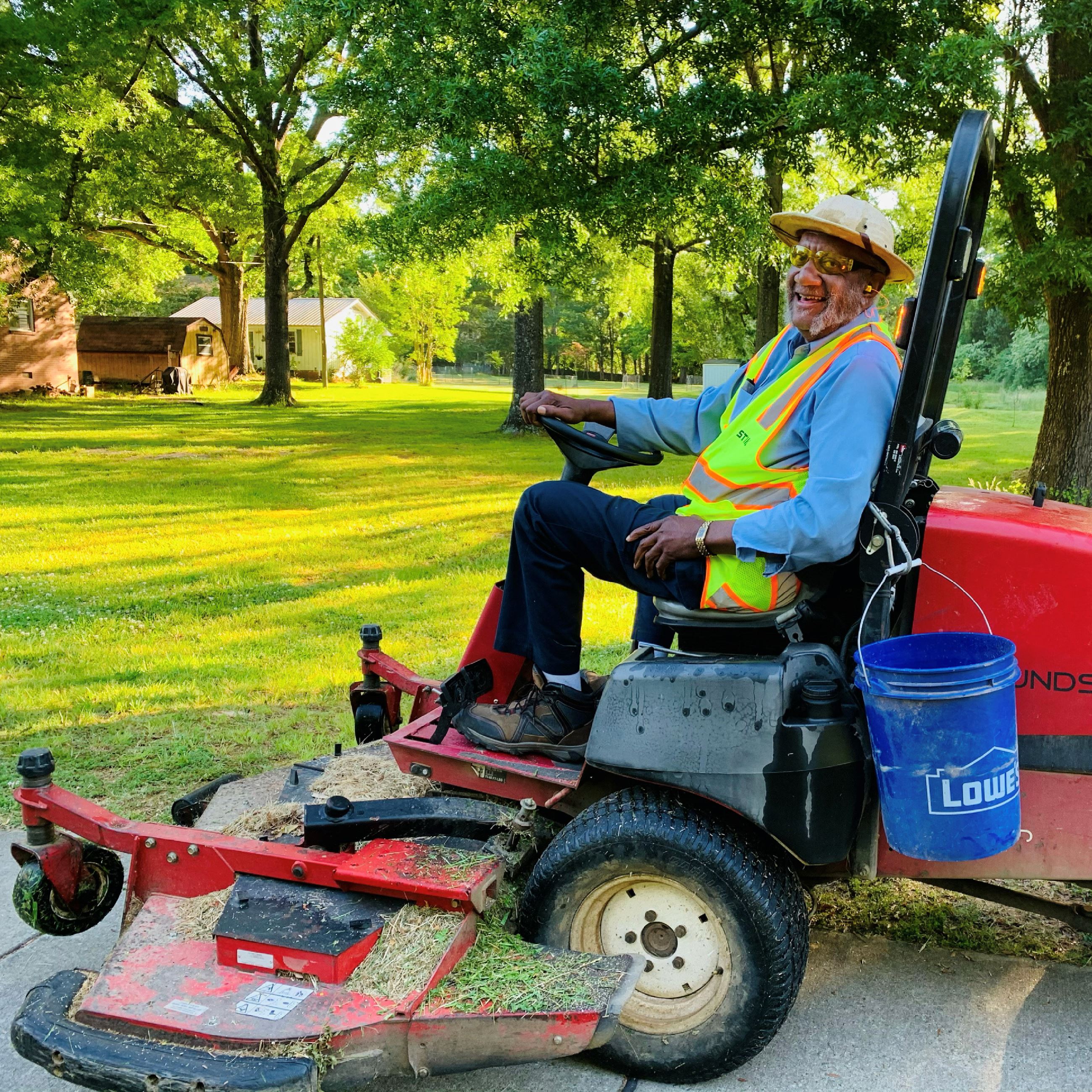 Picture shows a Public Works employee on a riding lawn mowing